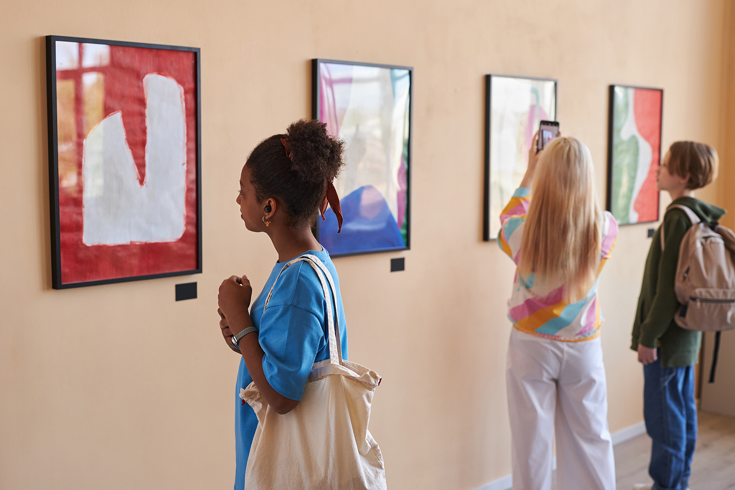 Diverse group of teenagers looking at abstract art in art gallery or museum standing in row with African American girl in foreground